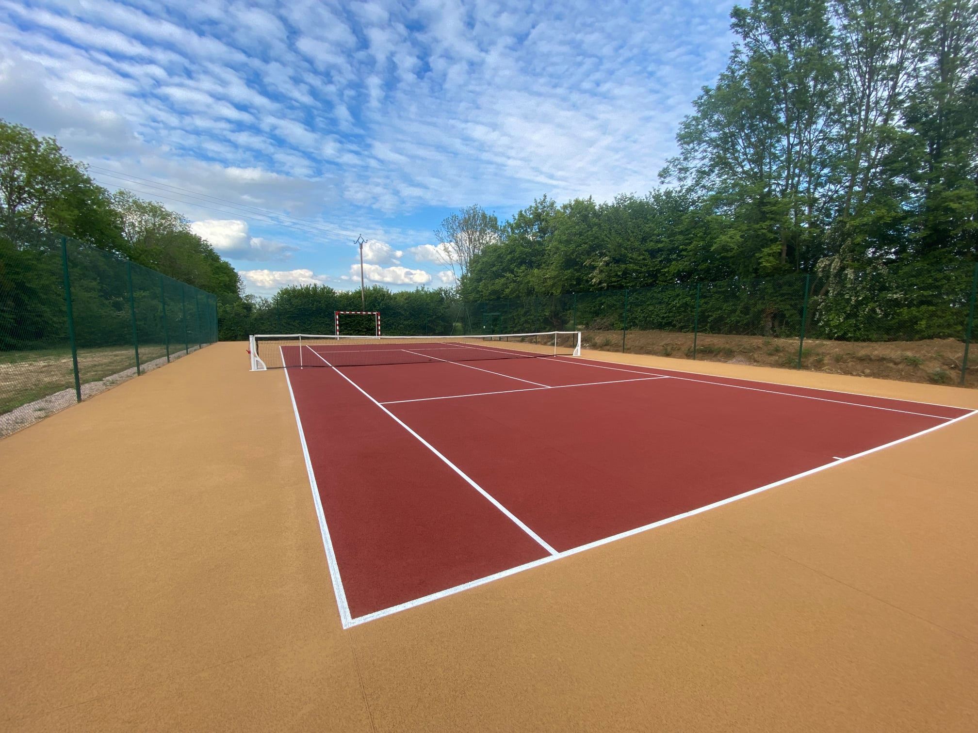 Terrain de tennis en béton poreux avec surface de jeu intérieure rouge et extérieure beige, idéal pour une expérience de jeu optimale.
