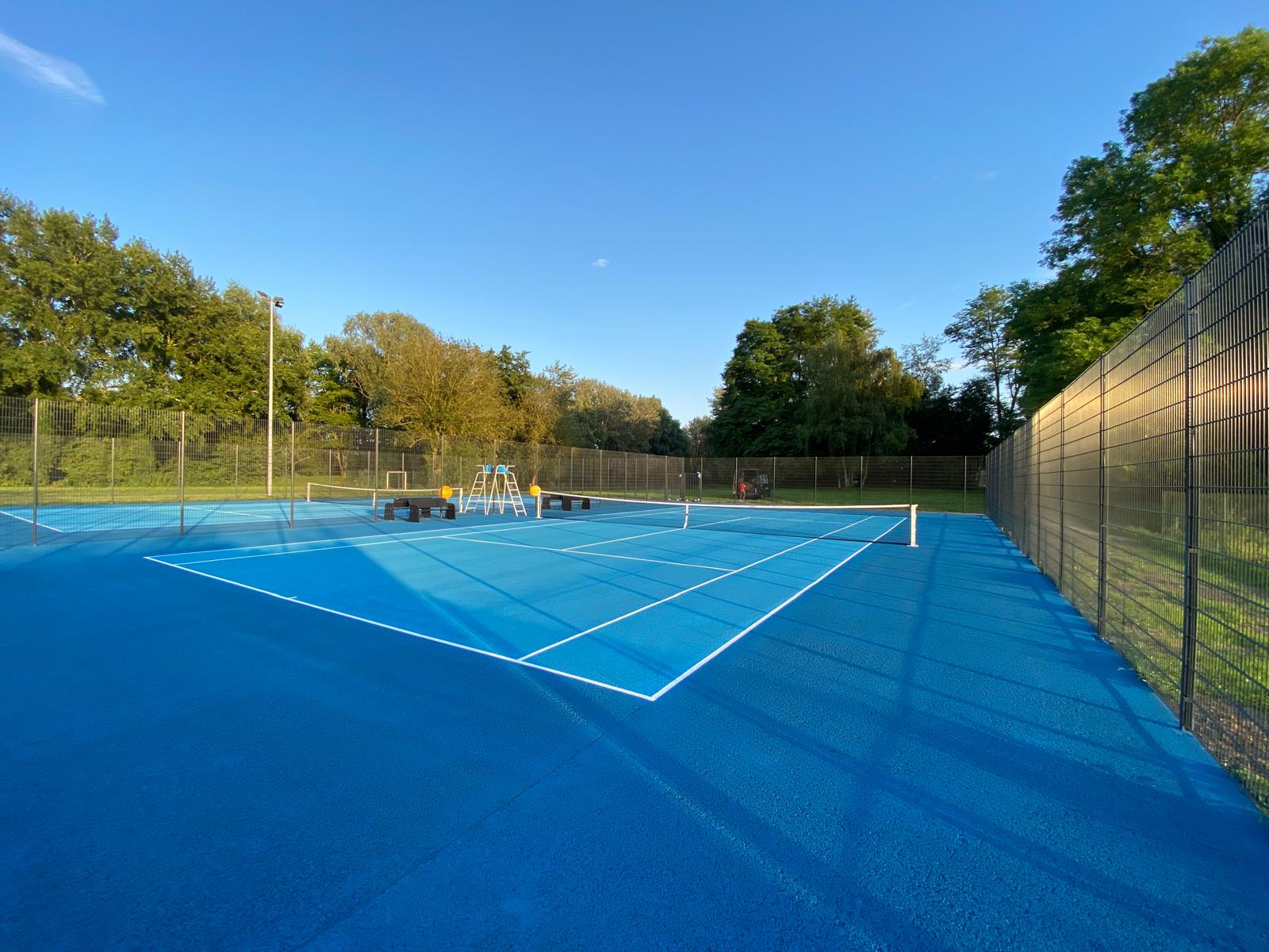 Image de deux courts de tennis en béton poreux avec des surfaces de jeu bleu clair et bleu foncé, conçus pour une performance et une visibilité supérieures.