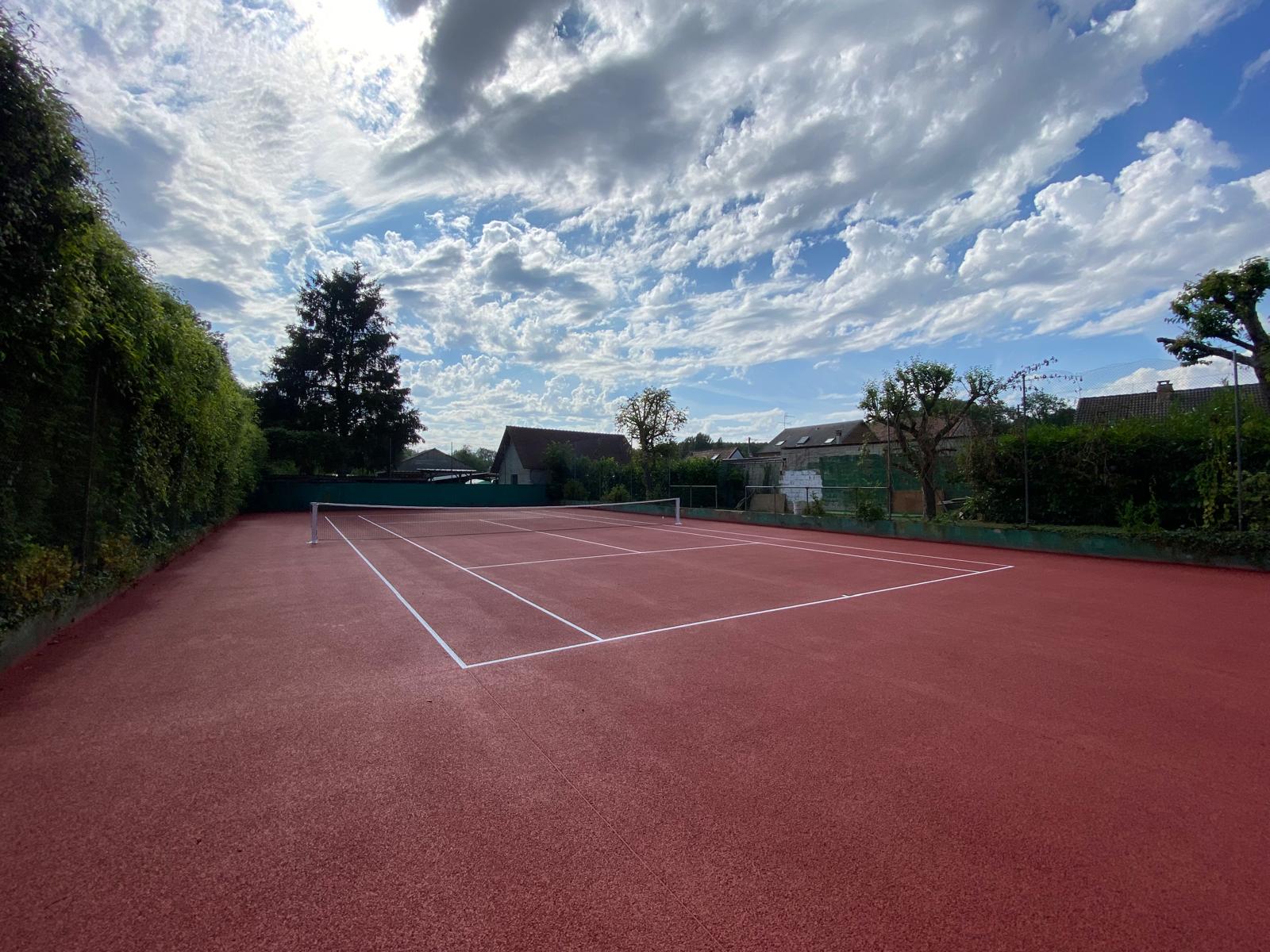 Court de tennis en béton poreux, tout en rouge, idéal pour une performance de jeu optimale.
